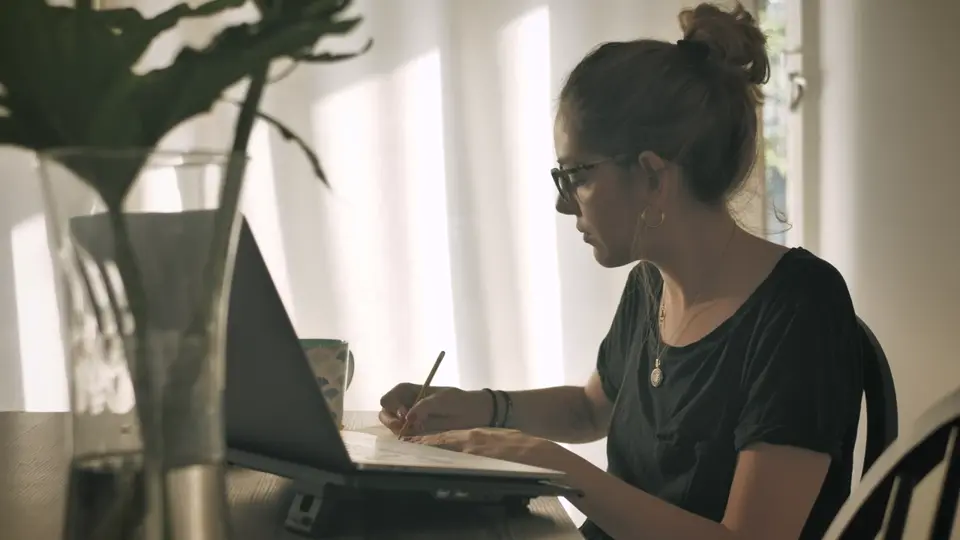 A woman working at a table by the window, still from a sample video